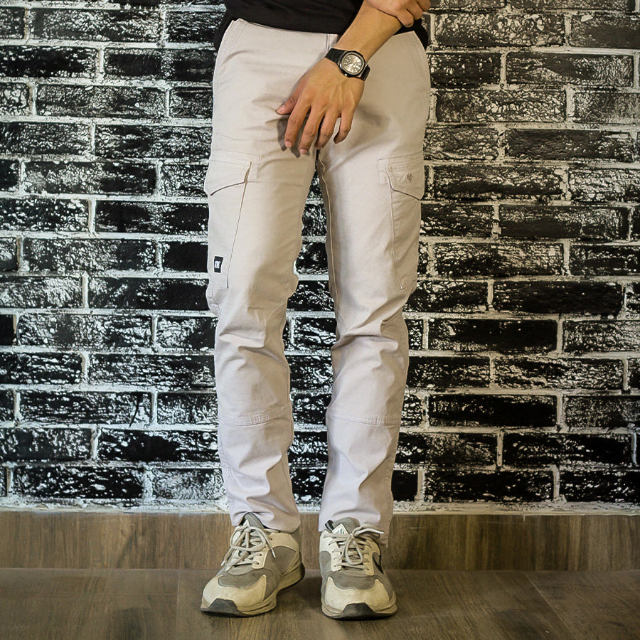 Person wearing a black t-shirt, white pants, and gray sneakers against a brick wall.