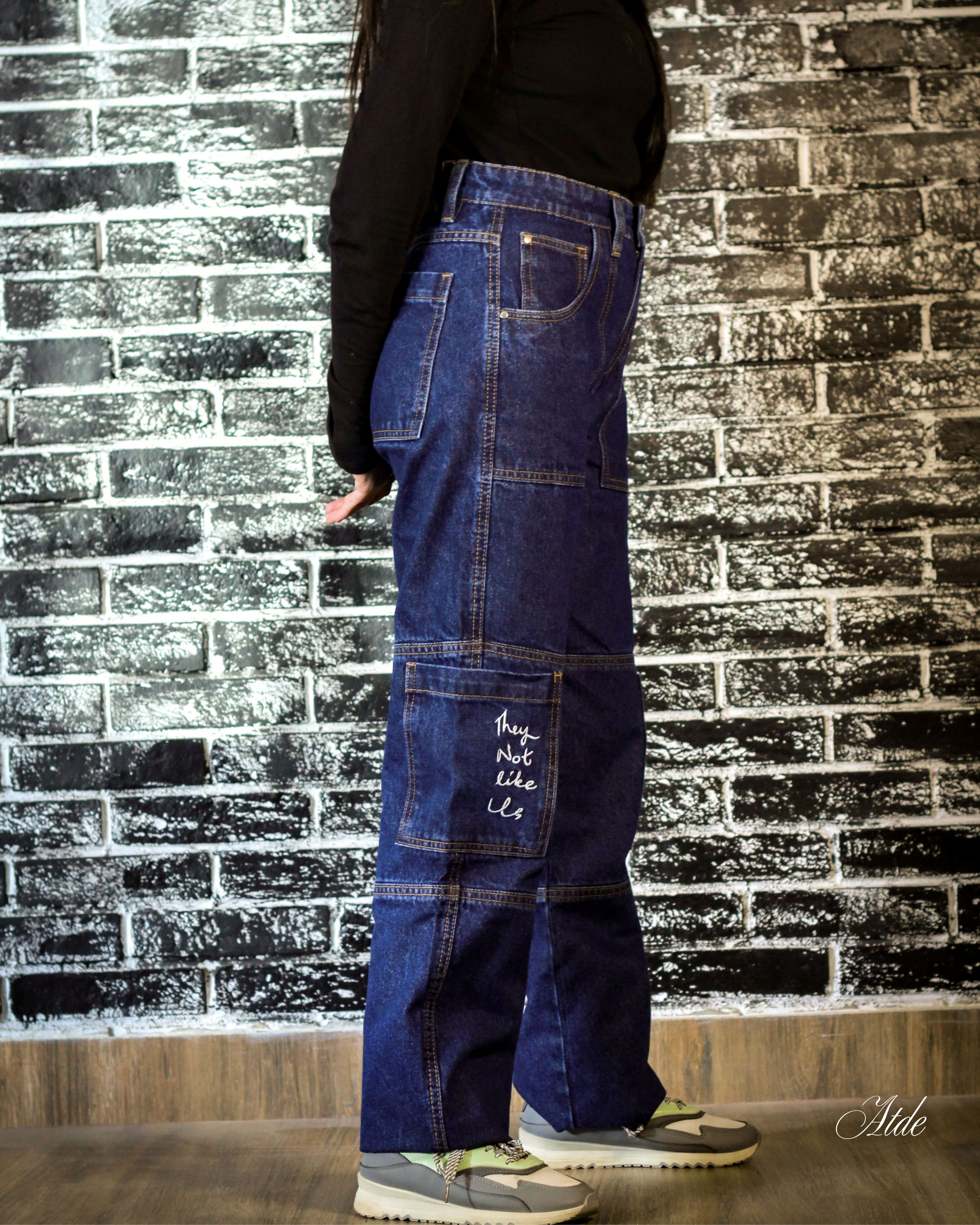 Person wearing blue patchwork jeans against a brick wall.