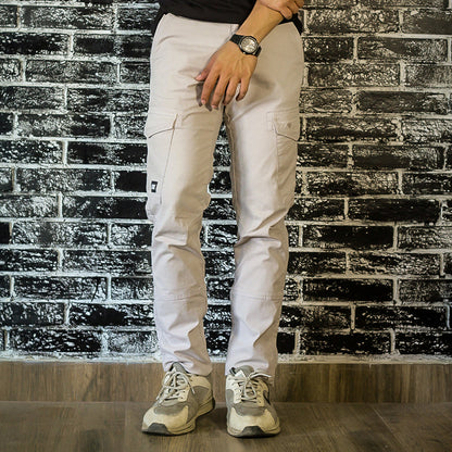 Person wearing a black t-shirt, white pants, and gray sneakers against a brick wall.